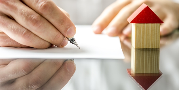 Person about to write on blank paper with wooden block house next to paper