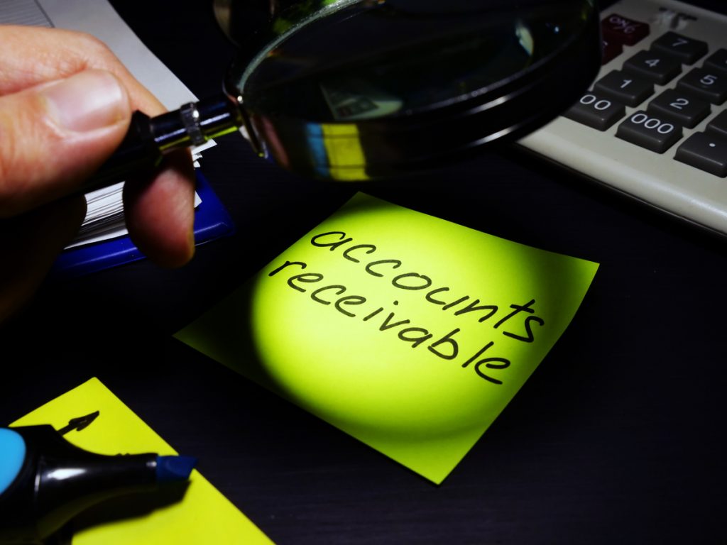 Magnifying glass examining sticky note with accounts receivable written on it.