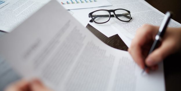 Image of businessman hand signing contract on table with papers and glasses nearby
