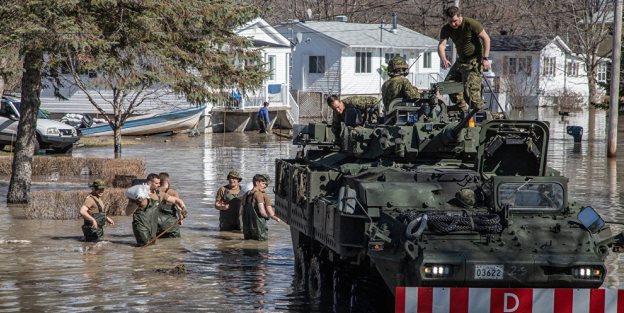 Army officers standing on military tank going through flooded residential area with people in flood