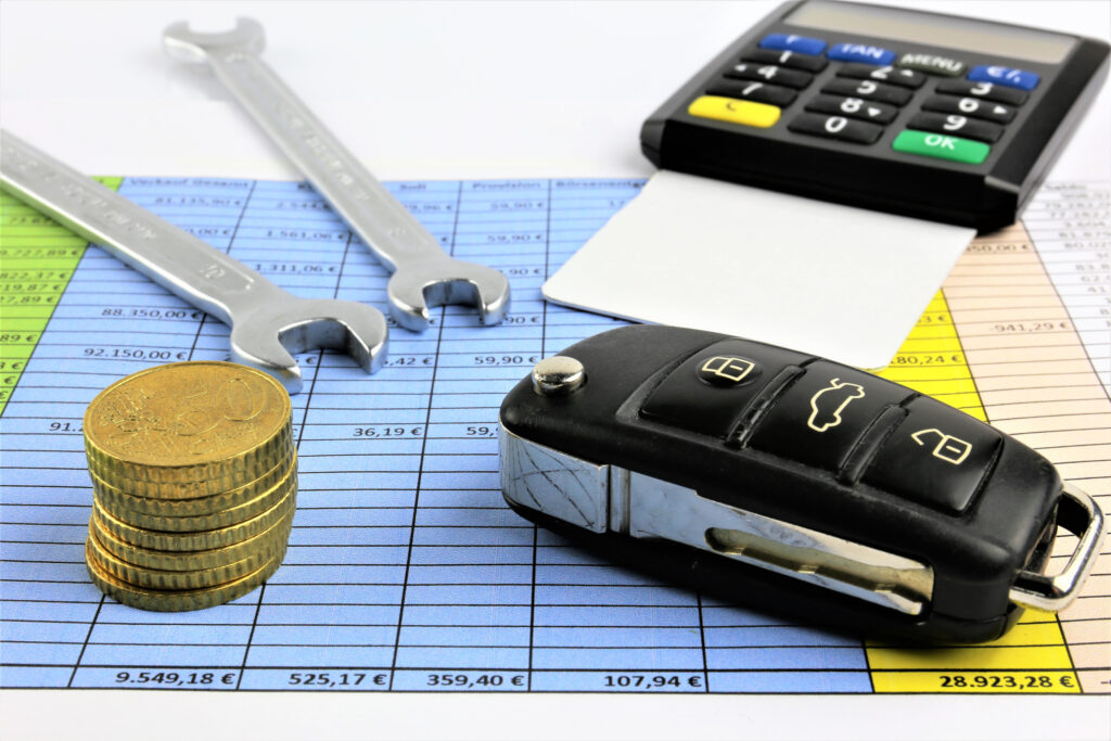 A concept image of car maintenance costs with keys, wrench, calculator and coins on financial spreadsheet