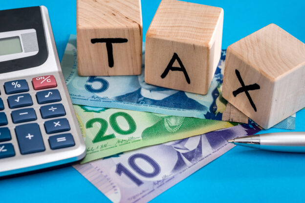 Wooden block letters spelling out tax on top of Canadian money and next to calculator