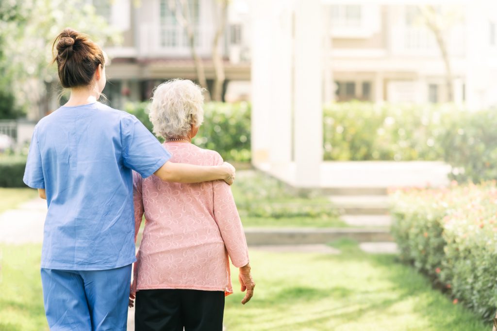 Medical pracitioner walks elderly patient outside of care home