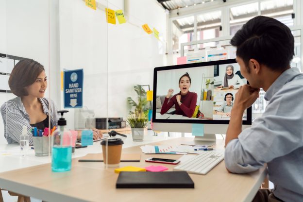 Staff in office meeting speak with other attendees on screen