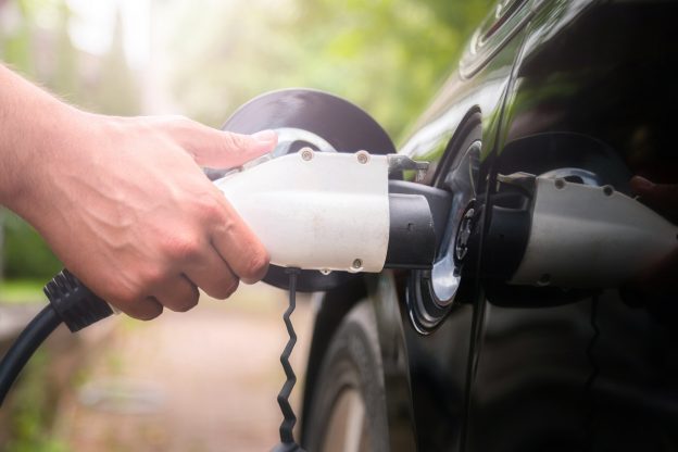 Hand plugging in electric car charger.