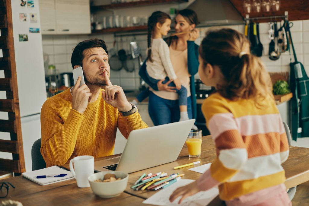 Family in kitchen while father tries to work from home