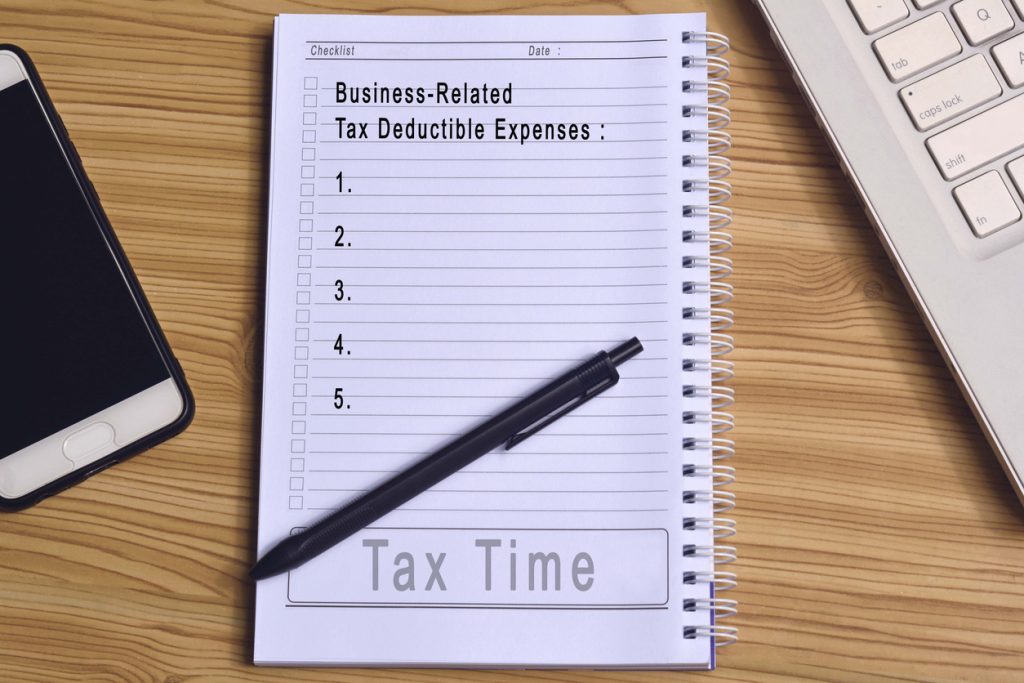 Text on notepad with laptop and smartphone on wooden table. Business and tax concept