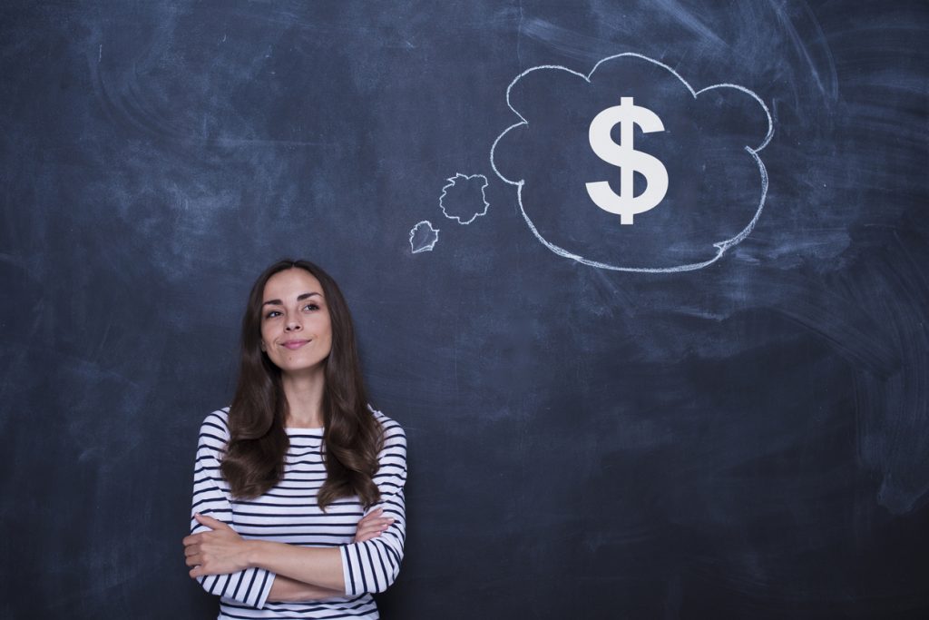Thoughtful confident businesswoman is standing near blackboard with large dollar sign drawn on it.
